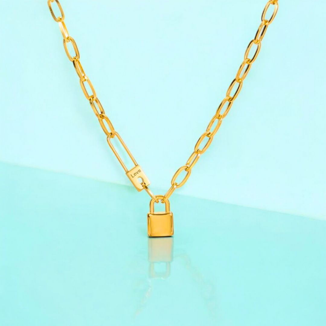 A gold-plated pin lock pendant on a chunky Cuban link chain necklace, displayed against a light blue background.