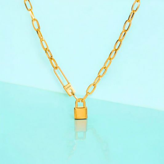 A gold-plated pin lock pendant on a chunky Cuban link chain necklace, displayed against a light blue background.